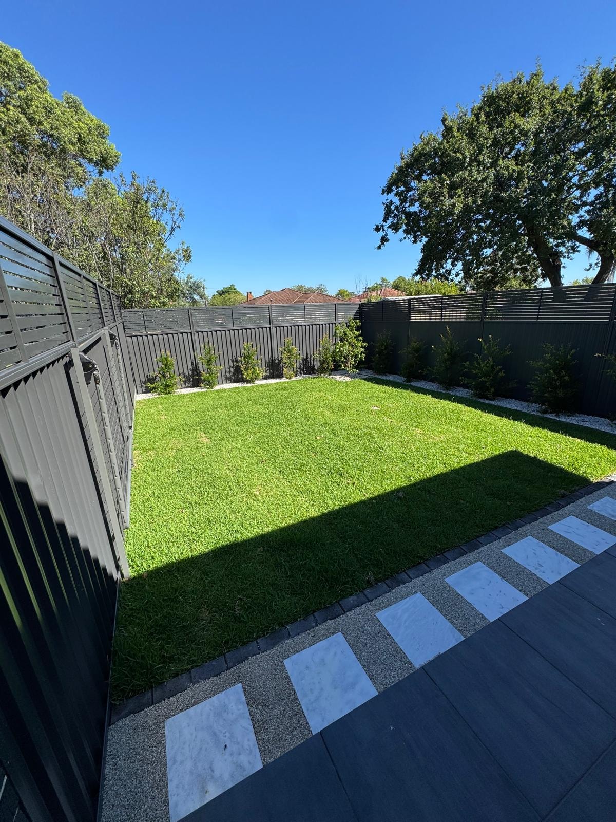 Backyard with lush lawn, stepping stone path and dark paving