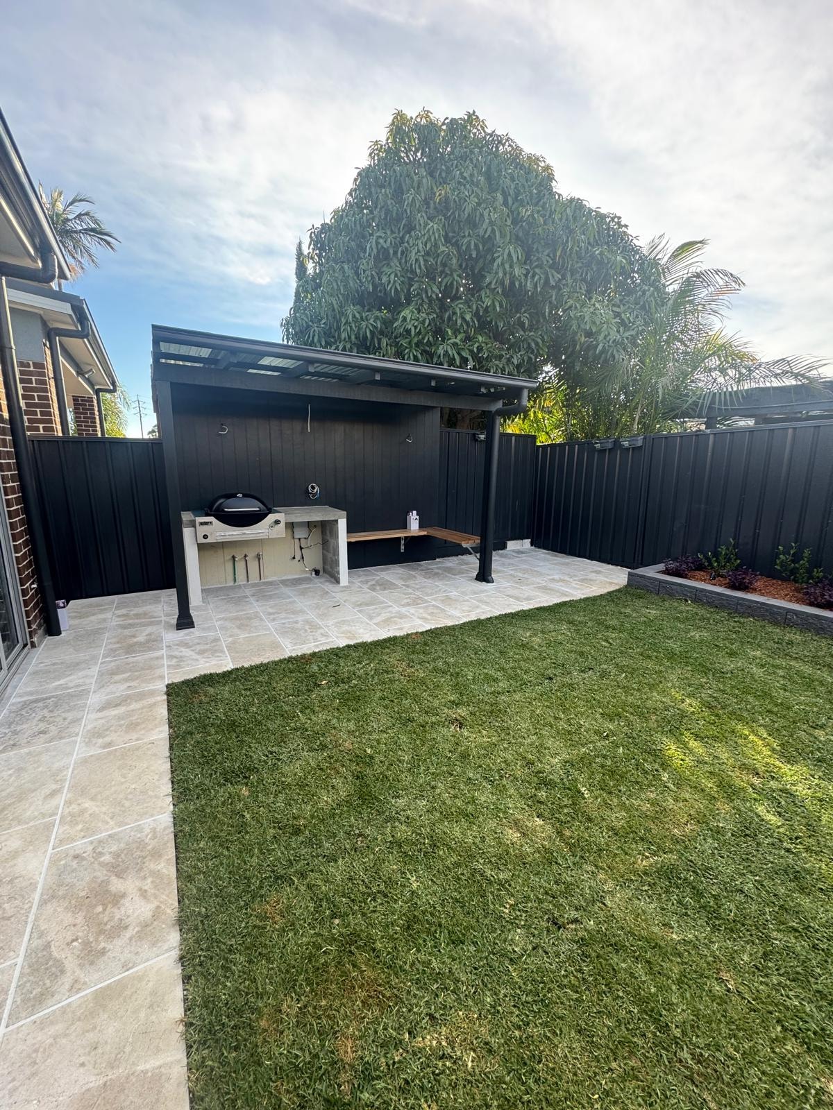 Black steel pergola with built-in BBQ, travertine paving and manicured lawn