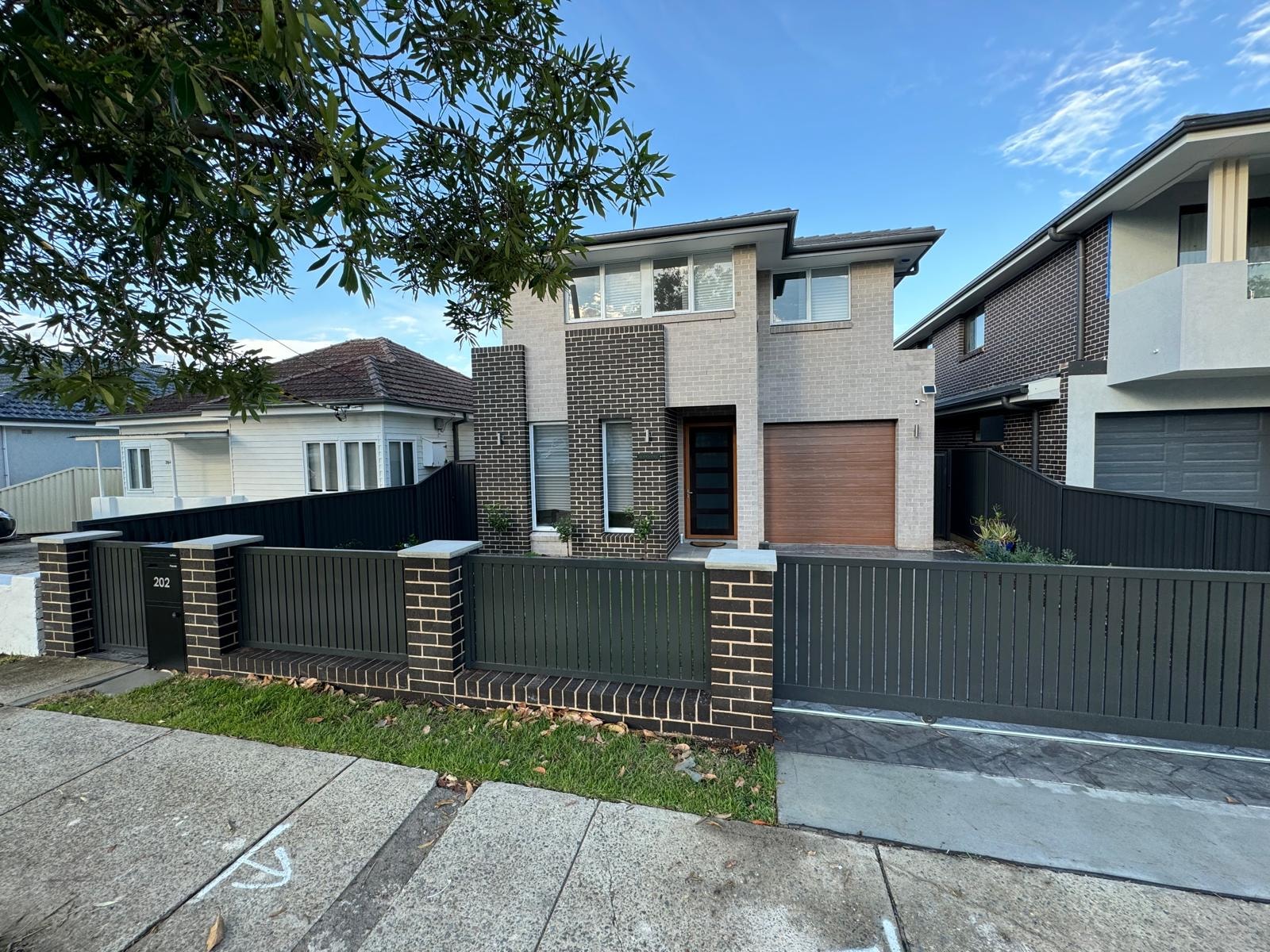 Modern brick home with charcoal slat fencing and landscaped driveway entrance