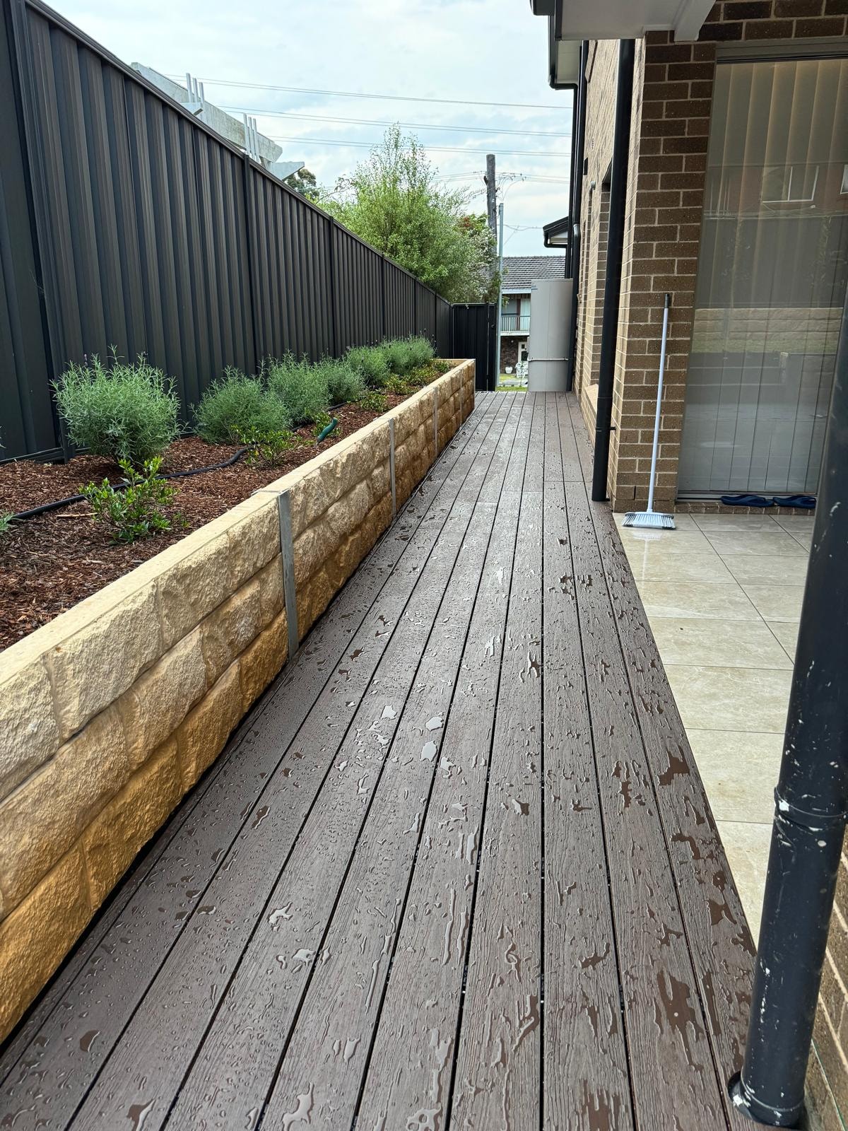 Composite deck running alongside sandstone retaining wall with herb garden bed