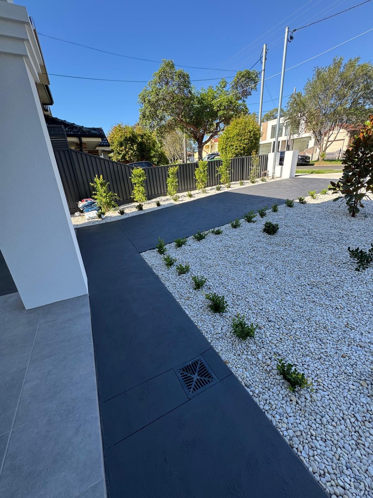 Dark paving pathway with white pebble garden beds and low plantings