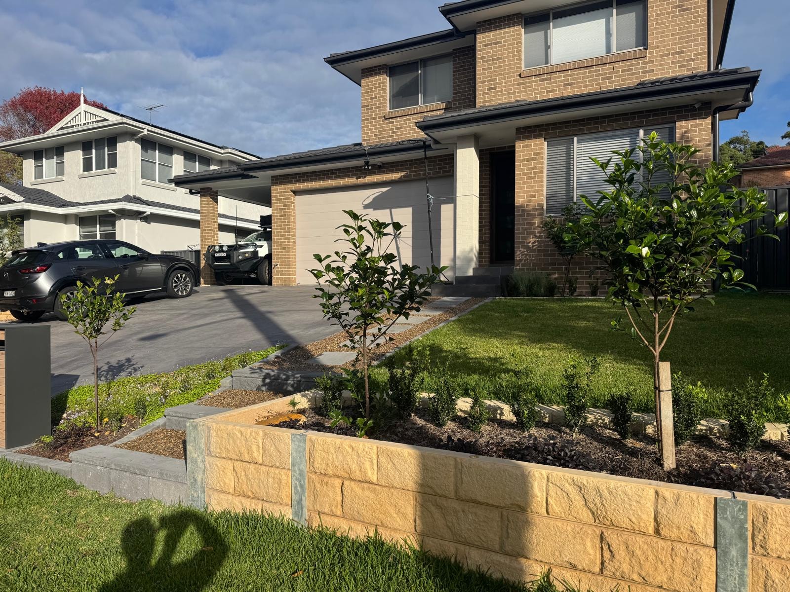 Front yard with sandstone retaining wall, garden beds and newly planted trees