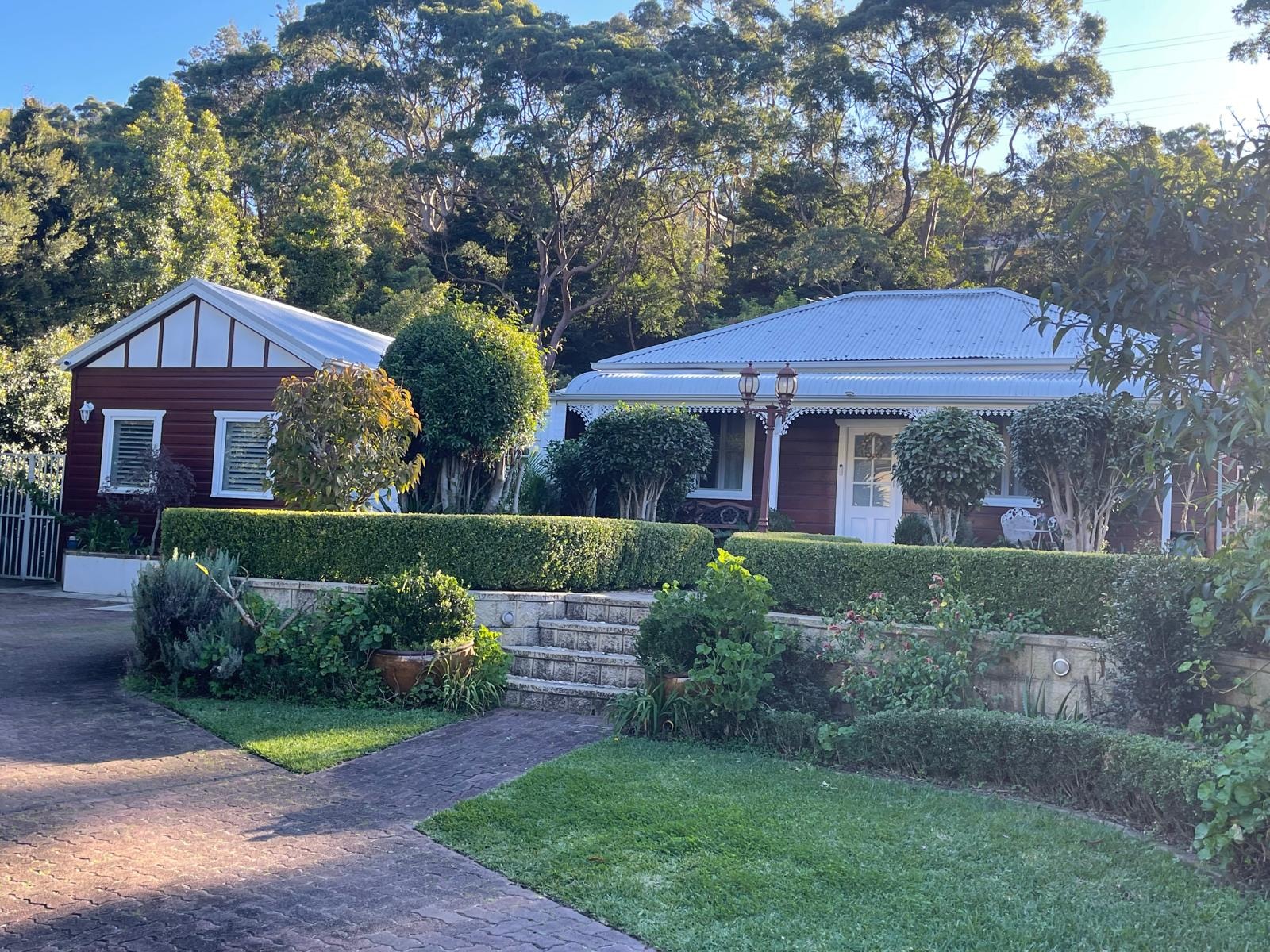 Heritage red timber home with manicured hedges, sandstone steps and lush garden