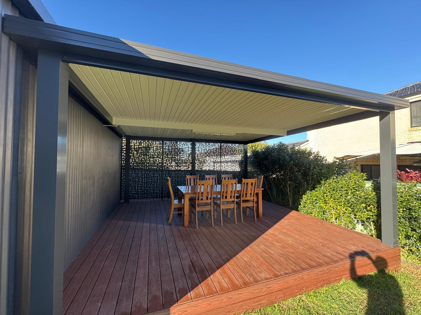 Charcoal louvre pergola with decorative screen panel over hardwood timber deck and outdoor dining