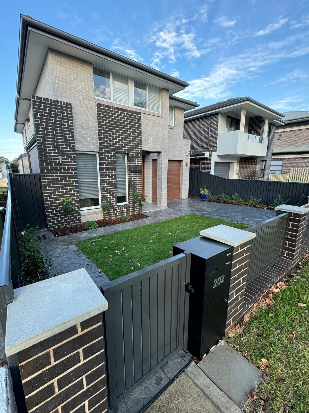 Modern home with charcoal front gate, brick fence and paved driveway