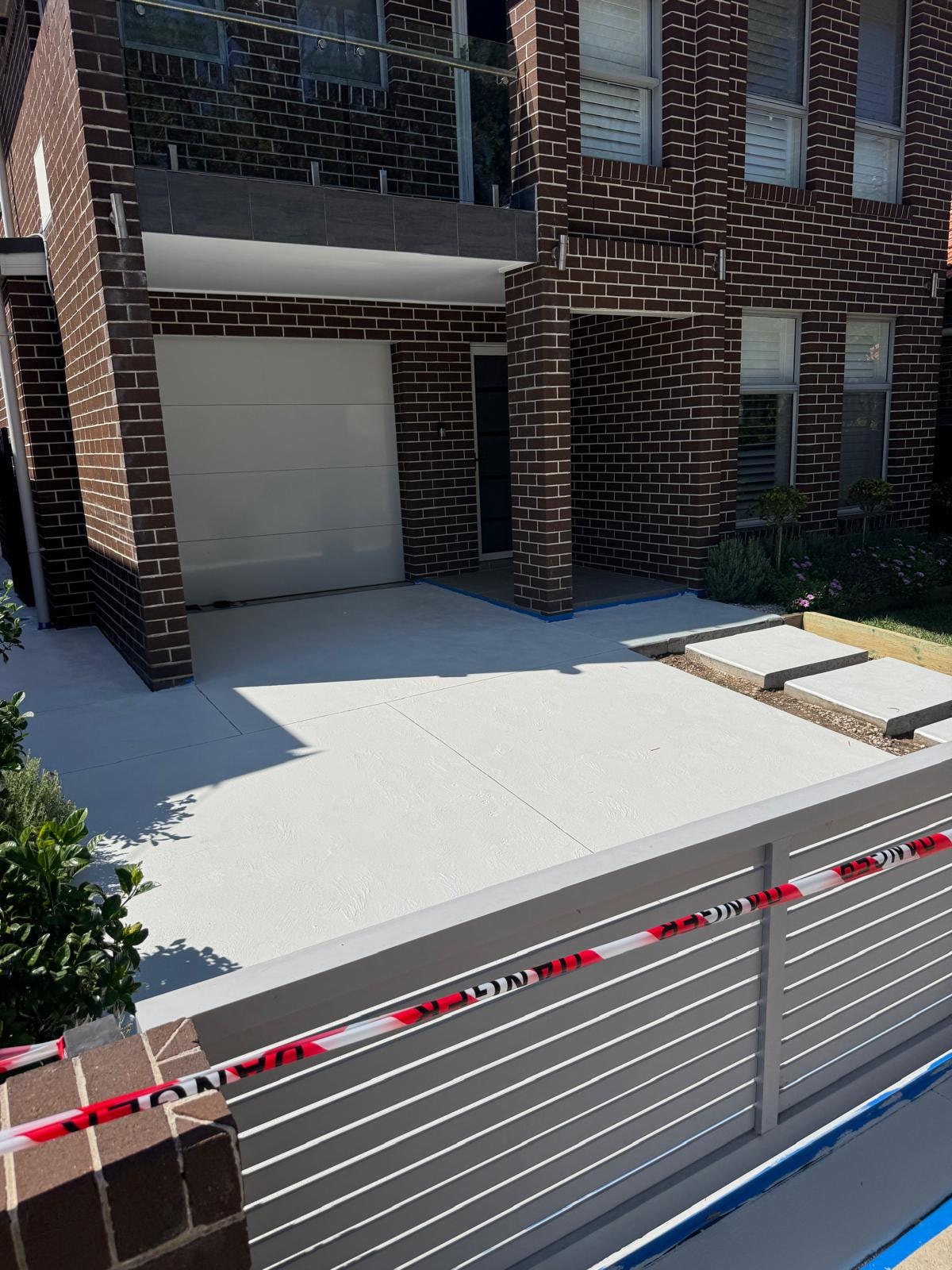 Freshly poured concrete driveway with charcoal slat fence at modern dark brick home