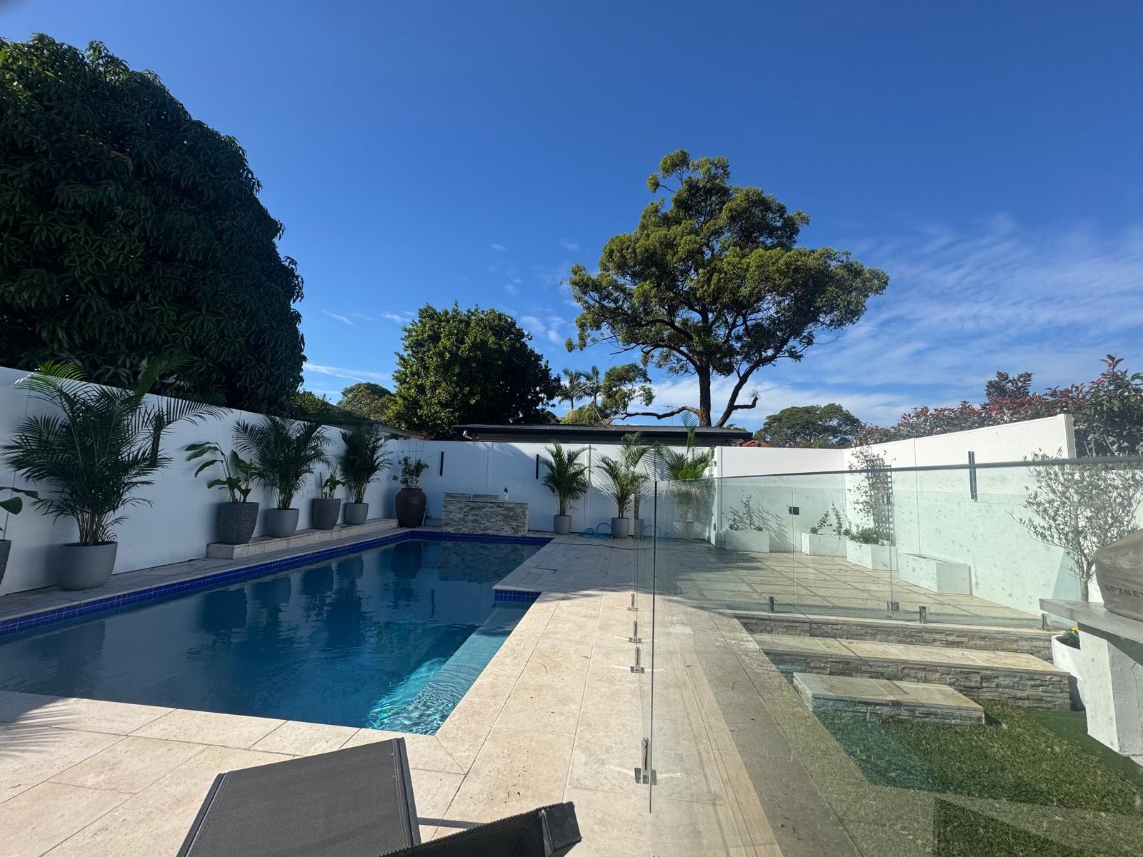 Completed pool area with glass fencing, travertine paving and tropical planting