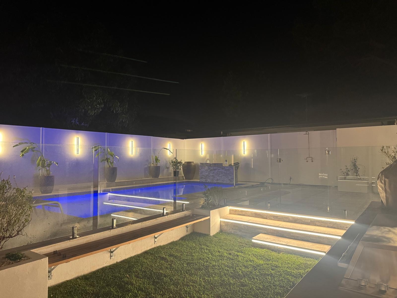 Pool area at night with LED step lighting and glass pool fence