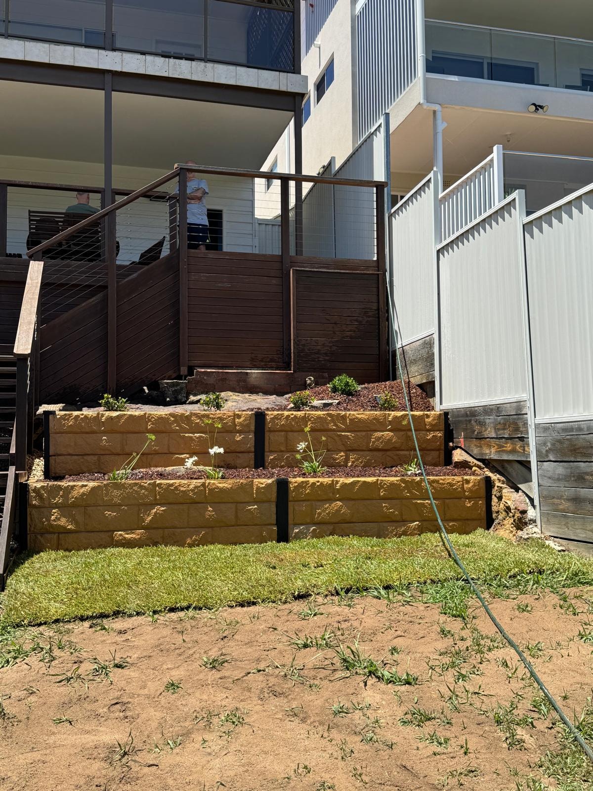 Tiered sandstone block raised garden beds with new planting beside timber deck and stairs