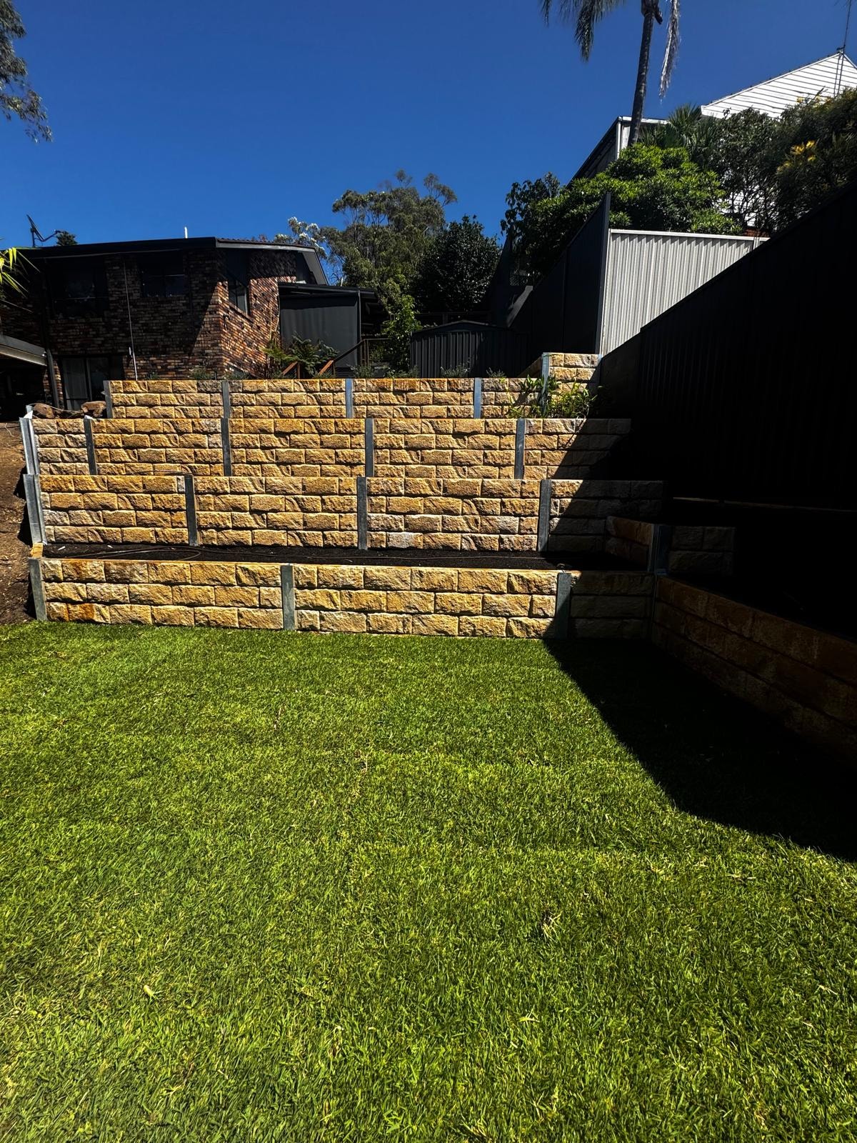 Sandstone block retaining wall with freshly laid lawn and garden beds