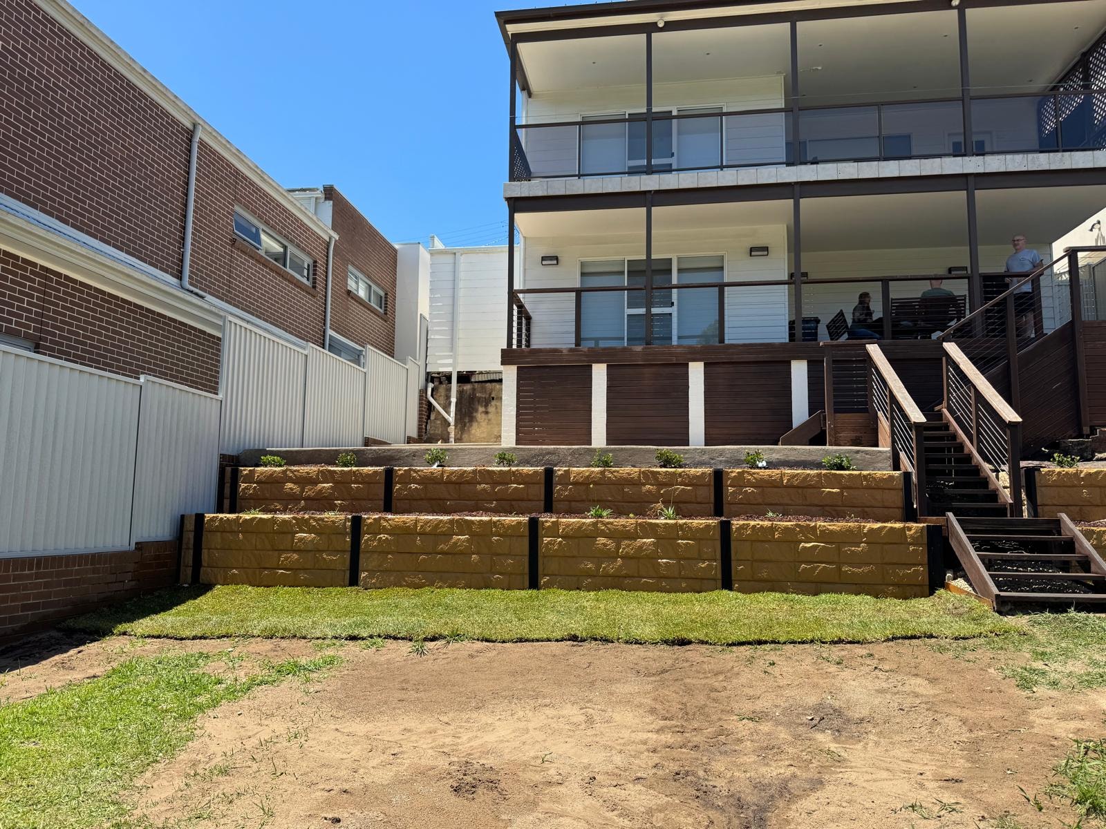 Wide sandstone block retaining wall with new turf and timber deck staircase
