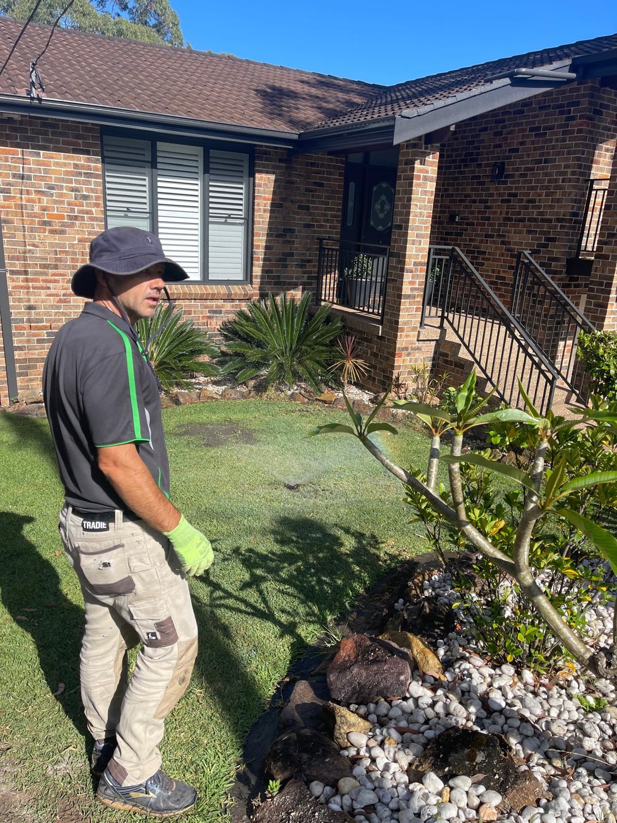 GPC Landscapes team member tending garden bed with white pebbles and tropical plants at brick home