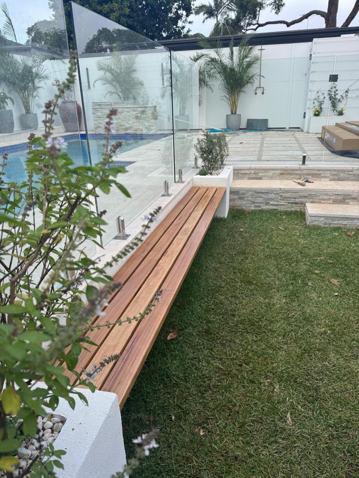 Hardwood timber bench seat beside glass pool fence with lawn and stone steps